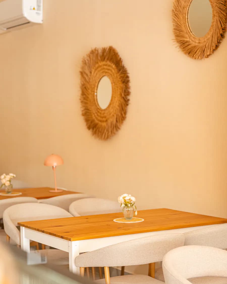 Dito Innenraum — Holztisch, beige Stühle, Rattan-Sonnen-Spiegel, Pfirsich-Lampe